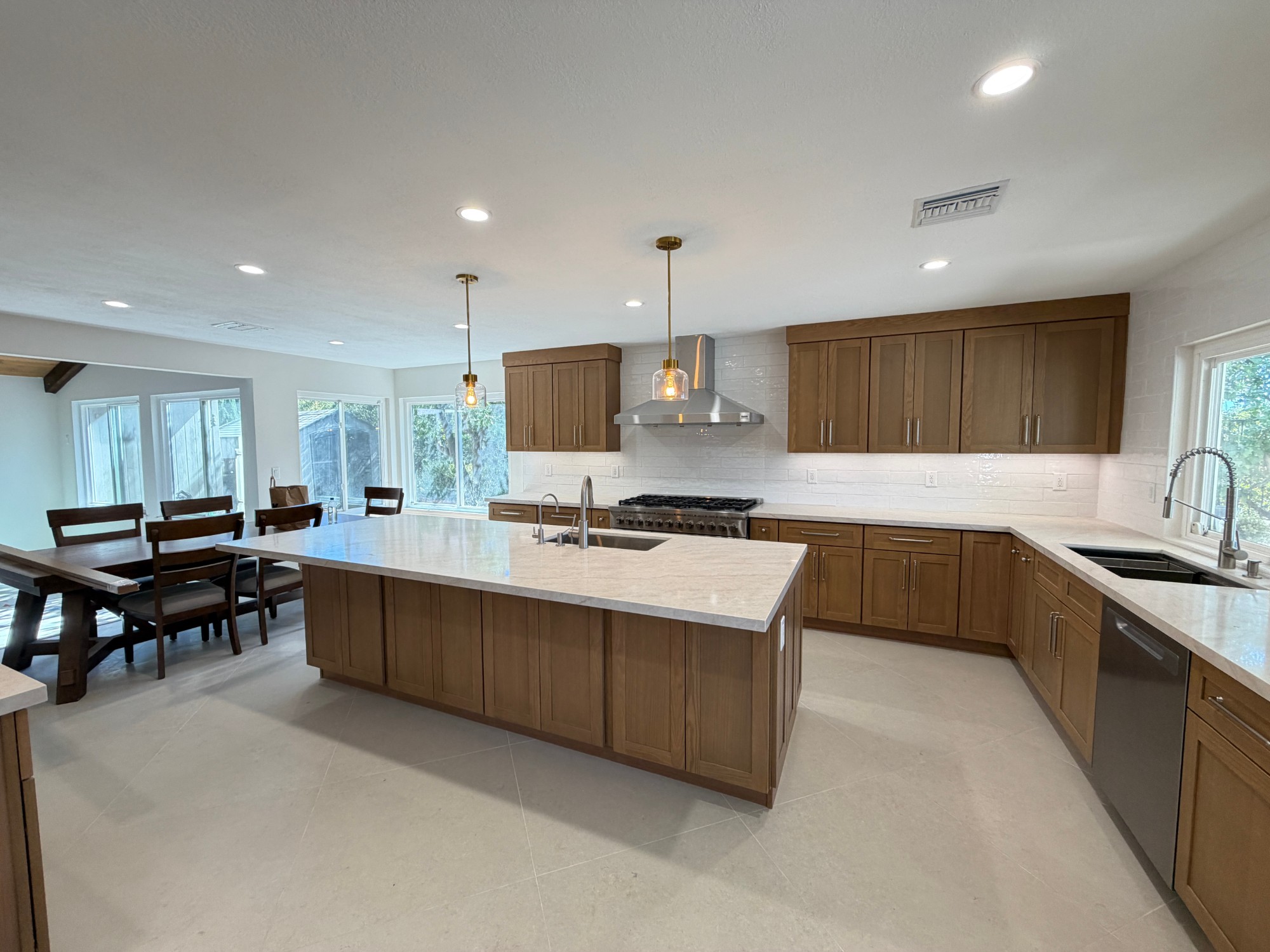 After: kitchen remodel by ValleyBuild with a large quartz island, custom wood shaker cabinets, stainless range hood and full-height tile backsplash